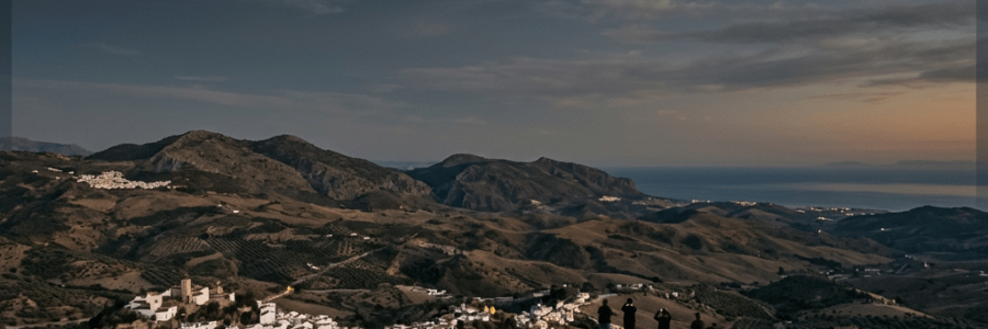 Partial solar eclipse over a mountainous landscape with a village and five people observing